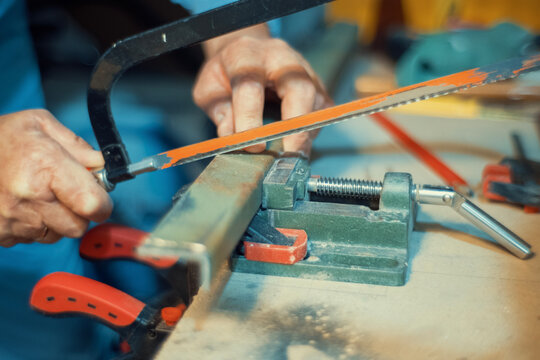 Close-up of a hand using a hacksaw to cut a metal piece clamped in a vise. Authentic metalworking photo for industrial, craft and maker projects