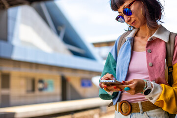 Railway theme. A beautiful young woman with a backpack holds a phone in her hand and waits for a train, standing on the platform. Tel Aviv, Israel. © zhukovvvlad