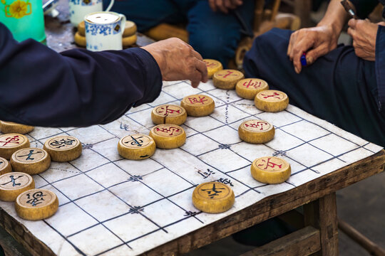 Chinese chess is played outdoor in front of a traditional tea house (On the chess pieces are Chinese characters for KIng, Advisors, General, Soldiers, Bishop, Chariot, Horse. etc.)