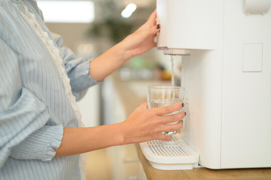 Woman Filling Glass from White Countertop Water Dispenser in Bright Domestic Kitchen