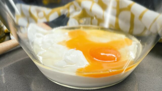 Close up of raw eggs cracked into a glass bowl, with broken yolks and egg whites prepared for mixing in a baking recipe. High quality 4k footage