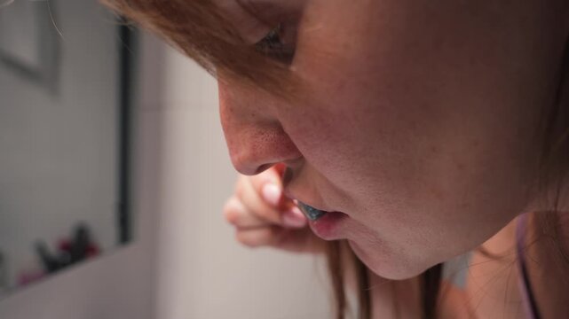 Close up of a woman brushing her teeth and spitting blood into a sink, showing bleeding gums and oral health problems. High quality 4k footage