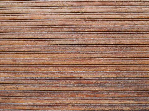 full-frame textured surface consisting of multiple narrow, horizontal brown wooden slats or panels arranged tightly parallel to each other, displaying a weathered natural grain pattern