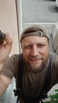 Vertical pov of Caucasian middle aged repairman holding screwdriver outdoors, smiling at camera. Ideal for home maintenance, renovation and window repair services