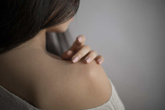 Southeast Asian woman touching her bare shoulder with gentle hand