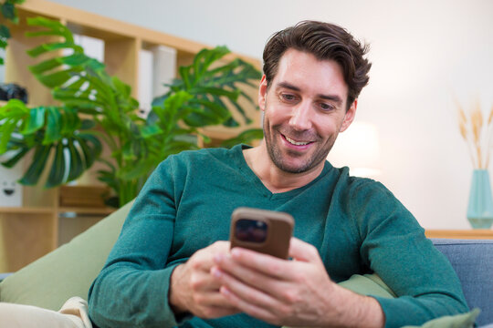 White man using smartphone in living room with plants and lamp