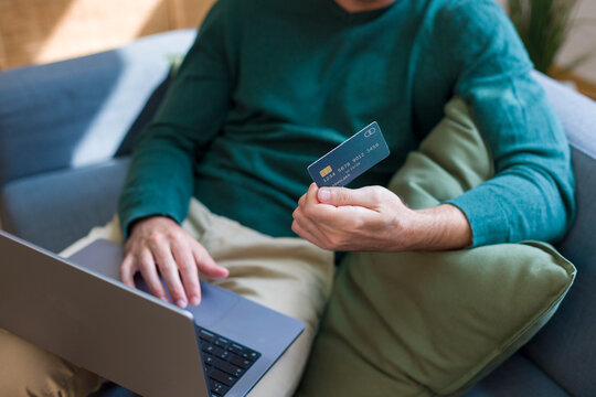 White person credit card using laptop on sofa at home