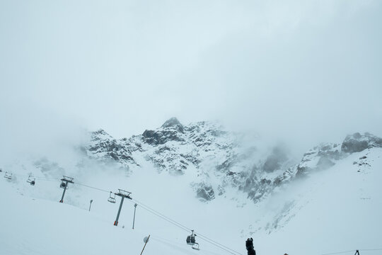 Snow-covered peaks loom in the background as ski lifts rise toward misty heights