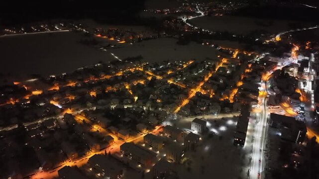 Night drone flight over the lights of the suburbs of Berne, Switzerland on a mystic winter night all covered with snow.