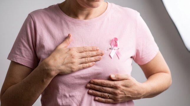 Woman performing breast self-examination in pink t-shirt with awareness ribbon, capturing proactive healthcare and early detection for medical marketing and oncology education.