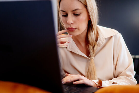 Woman browsing on a laptop while sitting on the sofa at home. Her hands near the keyboard, using the computer in the evening