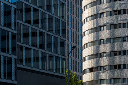 Rounded concrete facade beside dark glass office buildings in Wola Warsaw showing contrasting surfaces and repeating horizontal lines in a modern urban setting