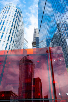Red translucent panels reflect glass towers in Wola Warsaw while a rounded white high rise stands behind the colorful architectural foreground in daylight