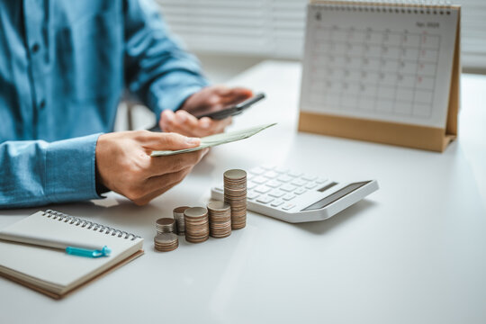 Money management with banknotes held beside a smartphone, coin stacks and calculator; money management for budgeting represented by cash and a calendar arranged on an indoor desk in a closeup view.