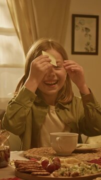 Portrait of cheerful Caucasian child removing sticky note from forehead during guessing game at dining table. Footage fits family lifestyle advertising and board game promotion, vertical