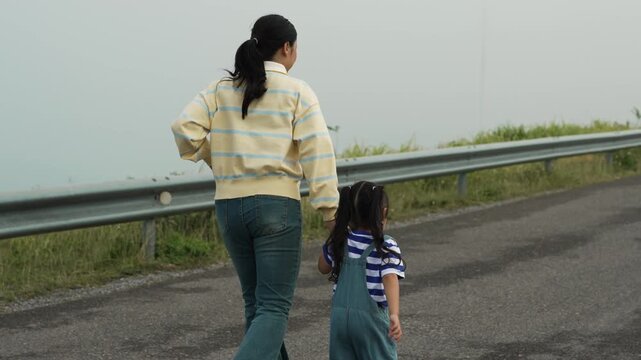 slow motion of mother and preschool child girl holding hand and running on a road on mountain in the morning