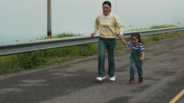 slow motion of mother and preschool child girl holding hand and running on a road on mountain in the morning
