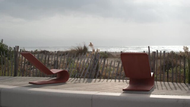 Terracotta lounge chairs on a sunlit seaside deck. Muted pastel colors, hazy white sky, and silvery sea, creating a dreamlike atmosphere of tranquility and meditative escape. 