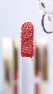 Red brush with water droplets dripping on it. Clear liquid flowing along the brush. Extreme front close up view with soft white background. Beauty tool concept.