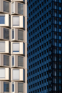 White geometric windows stand beside a dark blue glass tower creating contrast between two contemporary facades in modern urban architecture