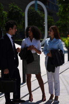 Diverse group of young professionals holding an impromptu stand-up meeting at the edge of a green mixed-use development, open gestures and easy body language, teamwork concept