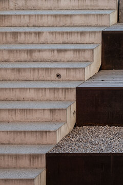 Pale concrete steps meet rust colored steel walls and a bed of gravel in a modern outdoor staircase defined by parallel architectural lines