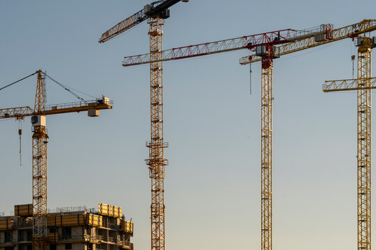 Several construction cranes rise above an unfinished building against a clear sky showing active urban development across a growing city skyline