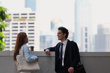 Fototapeta premium Business colleagues talking at a terrace wall with the city skyline behind them, a wide image of an outdoor break for corporate and property marketing, in soft hazy daylight