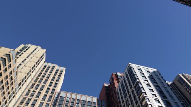 Camera tilts across varied high rise facades, revealing geometric windows and contemporary urban architecture against a cloudless blue sky