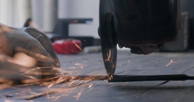 Close up view of hands operating angle grinder with flying sparks on worktable