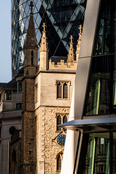 Historic stone church tower framed by contemporary glass buildings in London showing the contrast between traditional architecture and modern city development