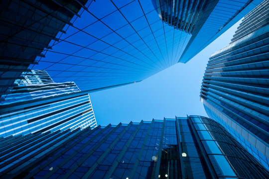 Blue glass skyscrapers rise around an open patch of sky in London creating a dramatic upward view of reflective facades and converging architectural lines