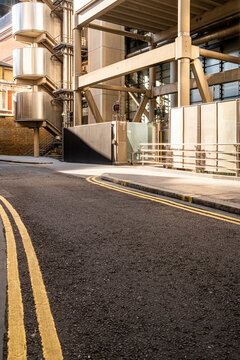 Curving asphalt street with double yellow lines beside exposed steel structures and mechanical architectural details in a modern business area of London