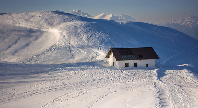A small, solitary cabin stands isolated among the hills covered in a blanket of white snow.