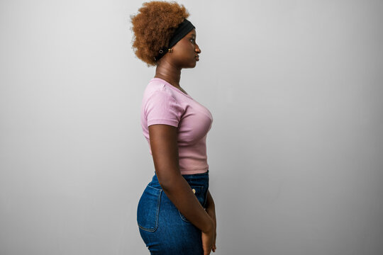 Young african american woman in pink clothes, side profile face with a confident natural pose, looking away with a warm smile &mdash; studio portrait of relaxed stylish woman