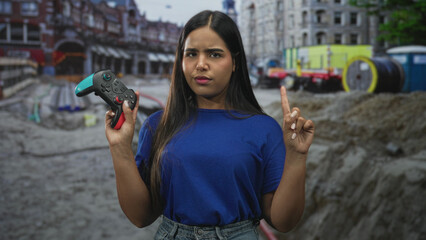 Young woman holds a gamepad with one hand and looks skeptical amid a street construction site  determination. © Krakenimages.com