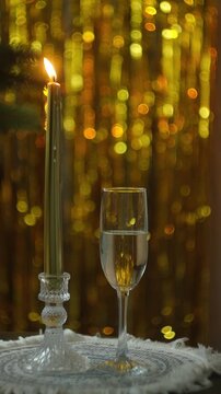 Vertical video. New year eve party. Glass of sparkling wine and burning candle on elegant golden background.