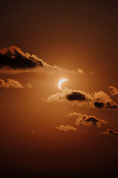Partial solar eclipse with dark clouds in an orange sky