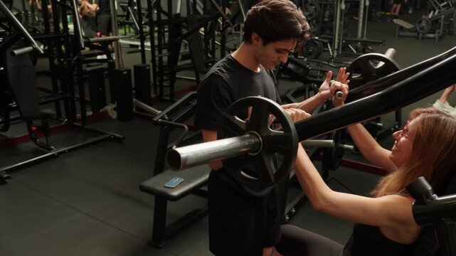 Young personal trainer showing a mature woman the correct technique on a plate-loaded gym machine, adjusting her grip for a safe and effective workout