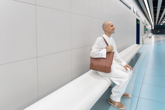 A bald man sits on a bench waiting in a modern subway station