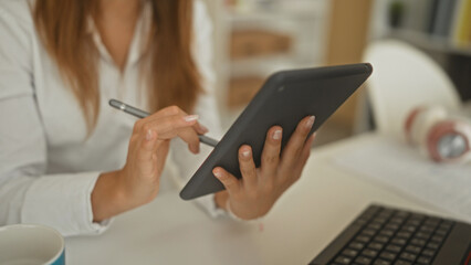 Woman holding tablet with stylus, fingers tapping screen at desk in building with coffee and keyboard nearby  focused productivity. © Krakenimages.com