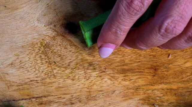 Closeup of Indian woman's hands cutting fresh green okra or bhindi with a kitchen knife on a wooden chopping board, preparing vegetables for traditional Indian cooking and homemade meals.