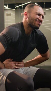Sick African American male man athlete feeling abdominal pain in gym during abs workout suffering digestive problem belly discomfort stomach ache unwell bodybuilder guy after fitness exercise indoors