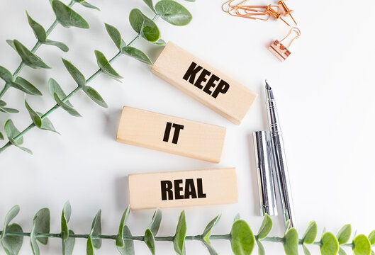 Keep it real text on wooden blocks with green leaves, pen and stationery on a white desk, authenticity concept