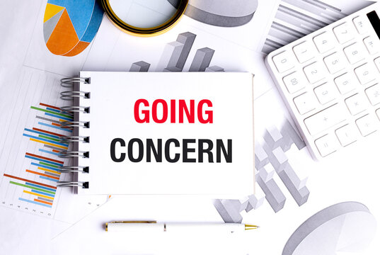 Going concern text on a spiral notebook with calculator, charts, pen and magnifier, accounting and business continuity concept