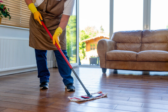 Person cleaning wooden floor in living room during day