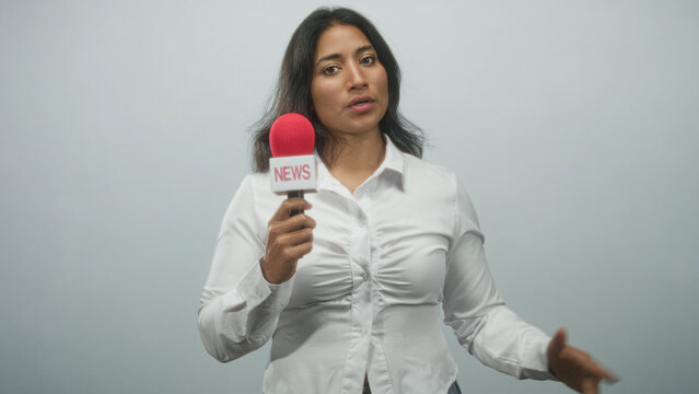 Woman holding a red microphone and gesturing with hand in a studio, wearing white blouse with neutral expression while speaking midshot; confidence authority.