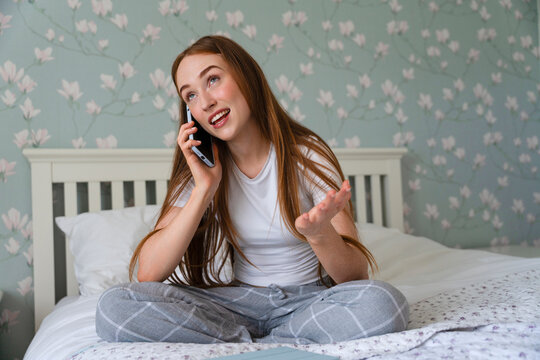Girl talking on the phone while sitting on bed in a decorated room with flower patterns