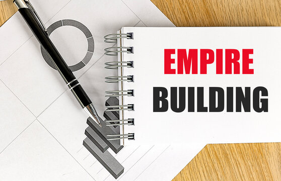 Empire building text on a spiral notebook with charts and pen on a wooden desk, business expansion, corporate growth