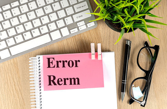 Misspelled text reading error rerm on pink paper clipped to a notebook, with keyboard, pen and glasses on a wooden desk